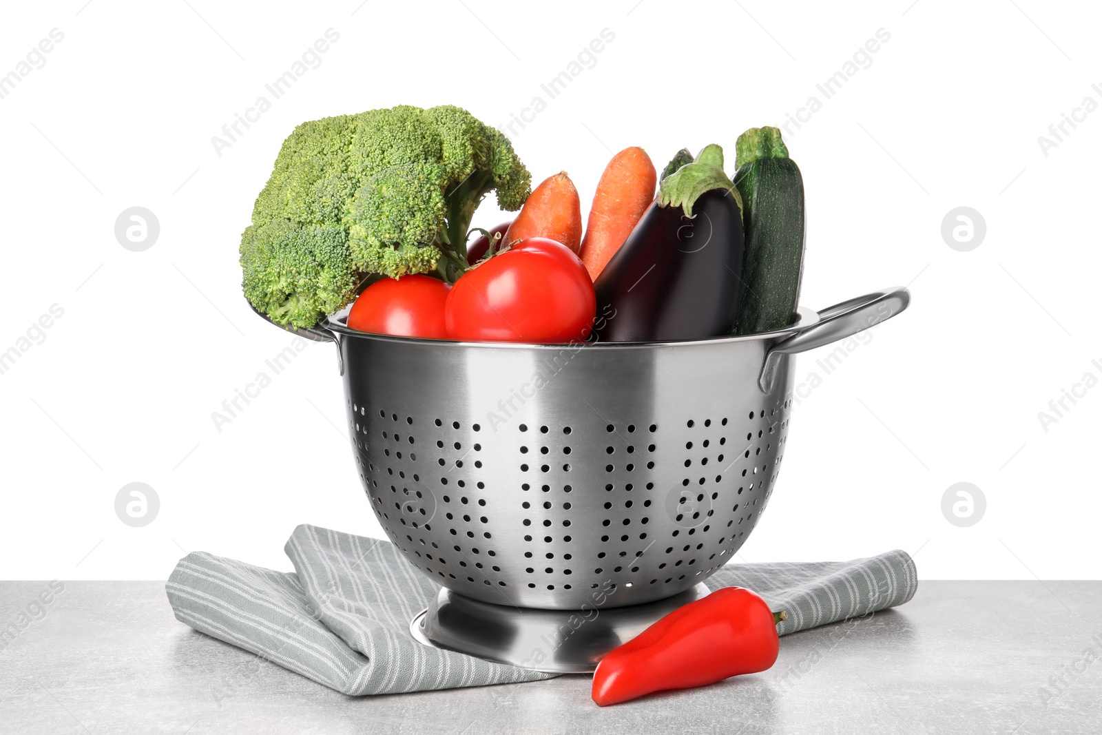 Photo of Different fresh vegetables in colander and napkin on table against white background