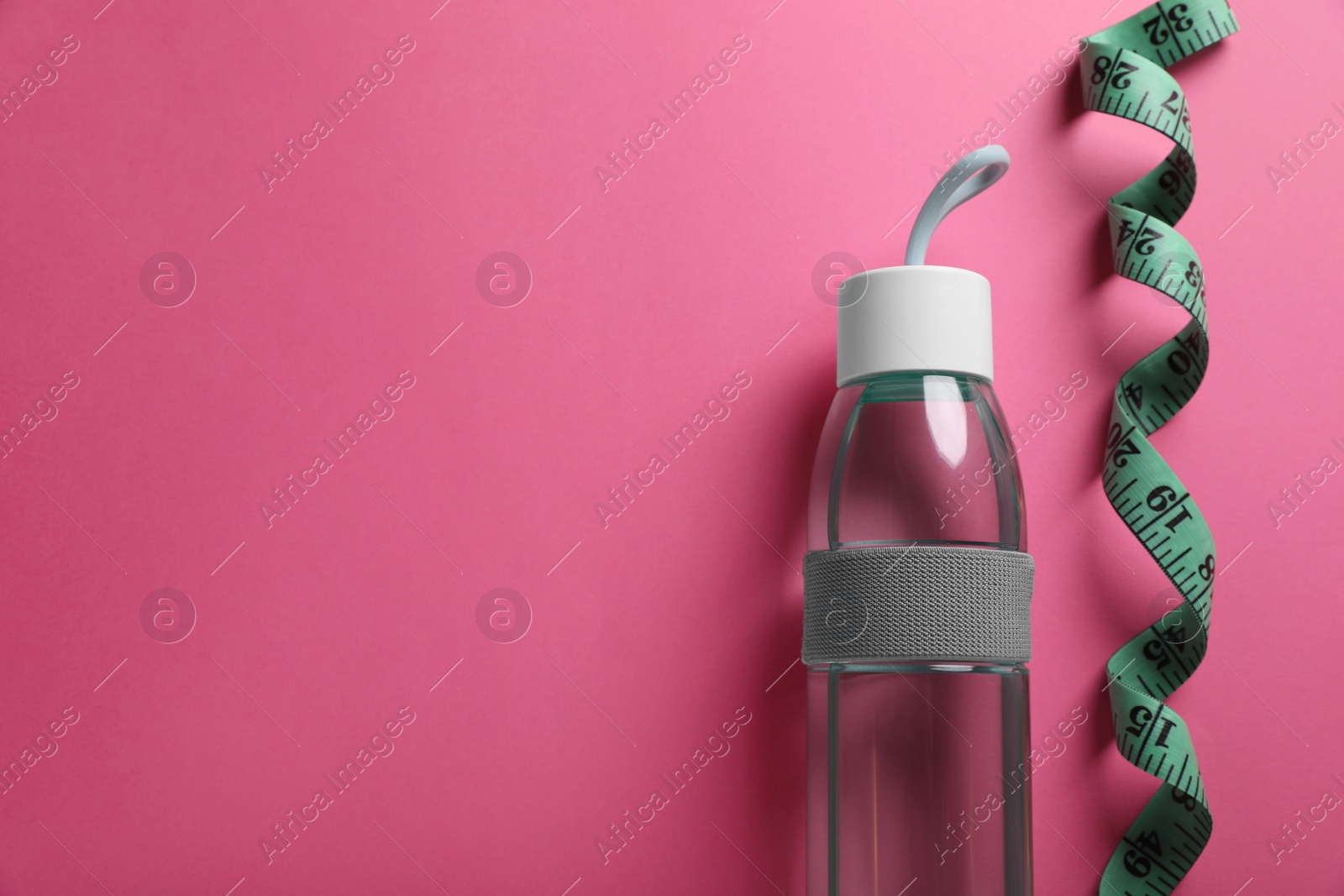 Photo of Measuring tape and bottle of water on pink background, flat lay with space for text. Weight control concept