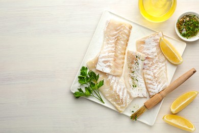 Photo of Fresh raw cod fillets with spices and lemon on white wooden table, flat lay. Space for text