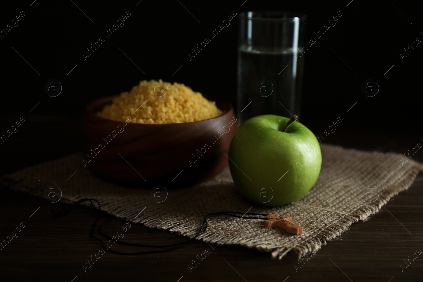 Photo of Millet, apple, water and crucifix on wooden table. Great Lent season