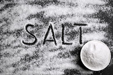 Photo of Word SALT and bowl on black background, top view