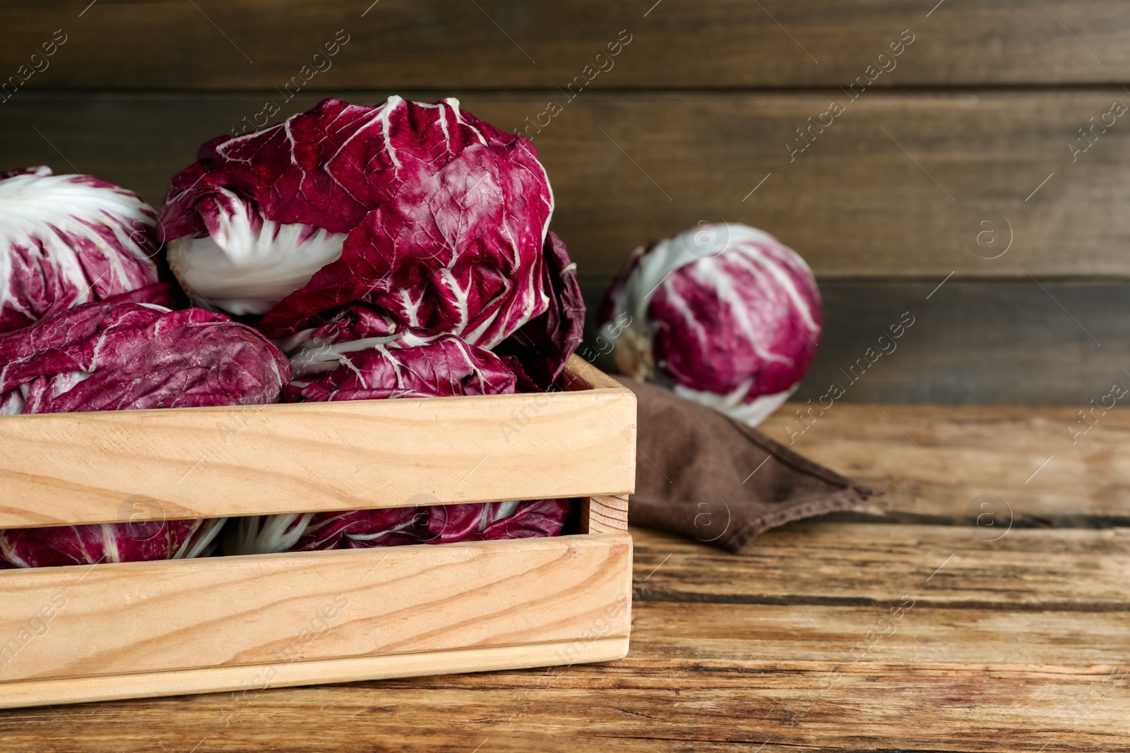 Photo of Fresh ripe radicchios in crate on wooden table, space for text