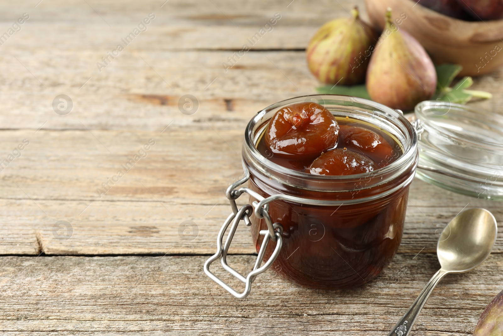 Photo of Jar of tasty sweet fig jam on wooden table. Space for text