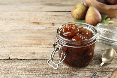 Photo of Jar of tasty sweet fig jam on wooden table. Space for text