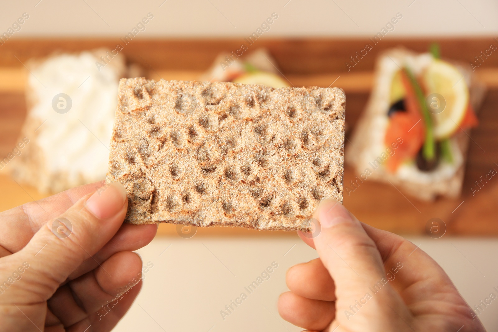 Photo of Woman holding fresh crunchy crispbread above table, closeup