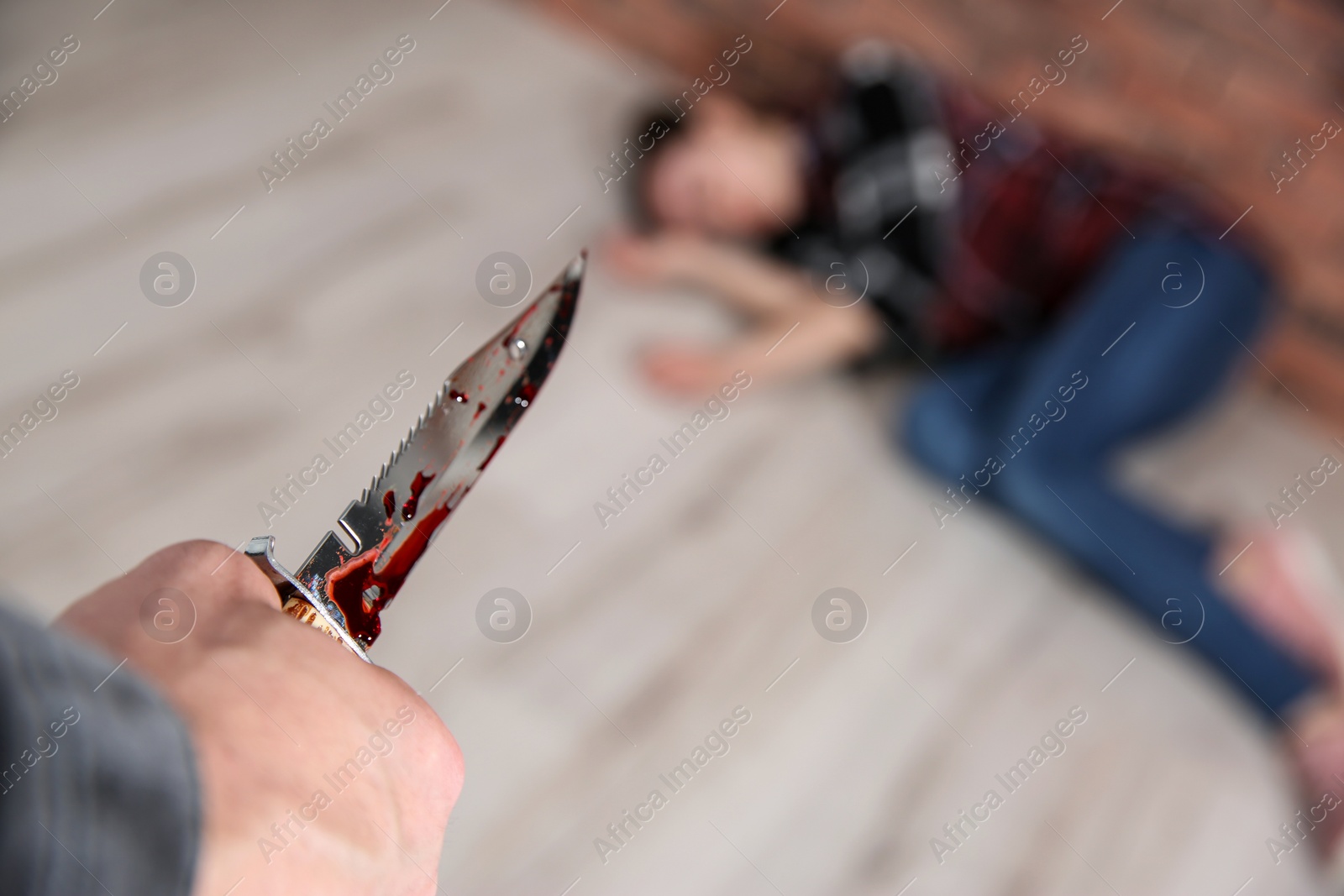 Photo of Man with bloody knife and his victim on floor indoors, closeup. Dangerous criminal