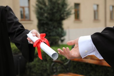 Student receiving diploma during graduation ceremony outdoors, closeup