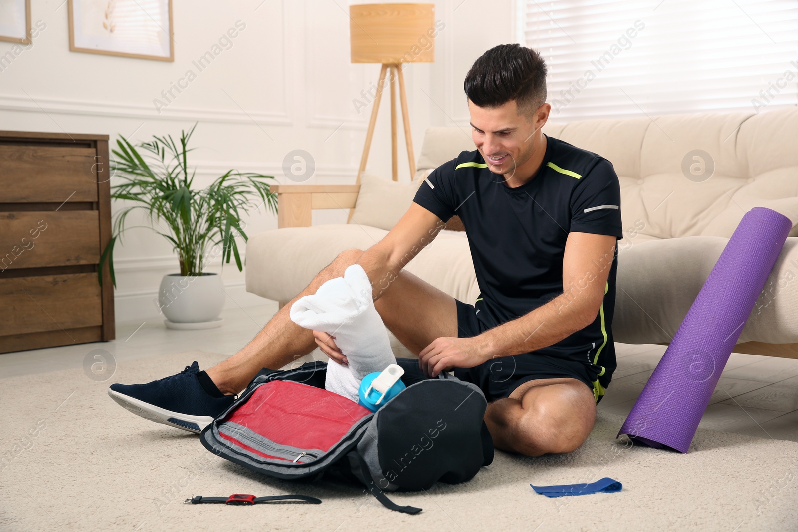 Photo of Man packing sports stuff for training into bag at home