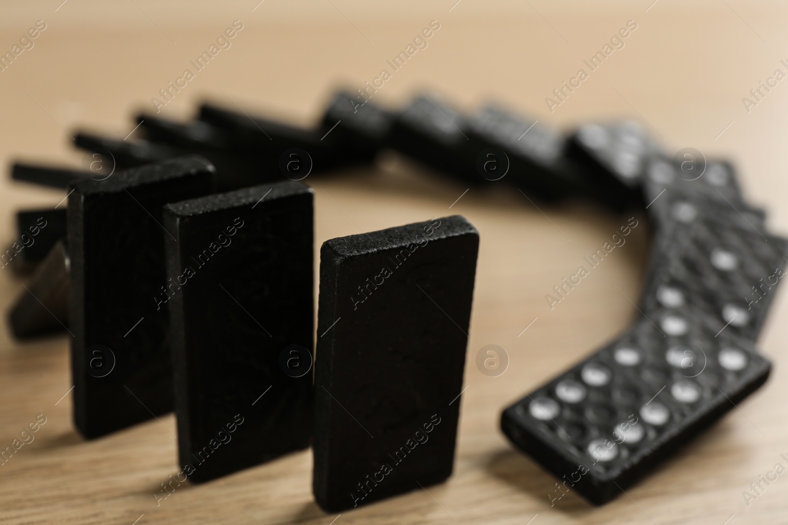 Photo of Black domino tiles falling on wooden table, closeup