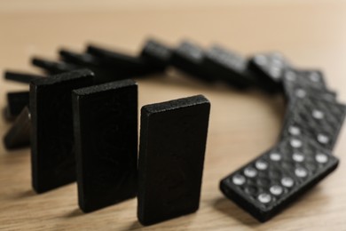 Photo of Black domino tiles falling on wooden table, closeup