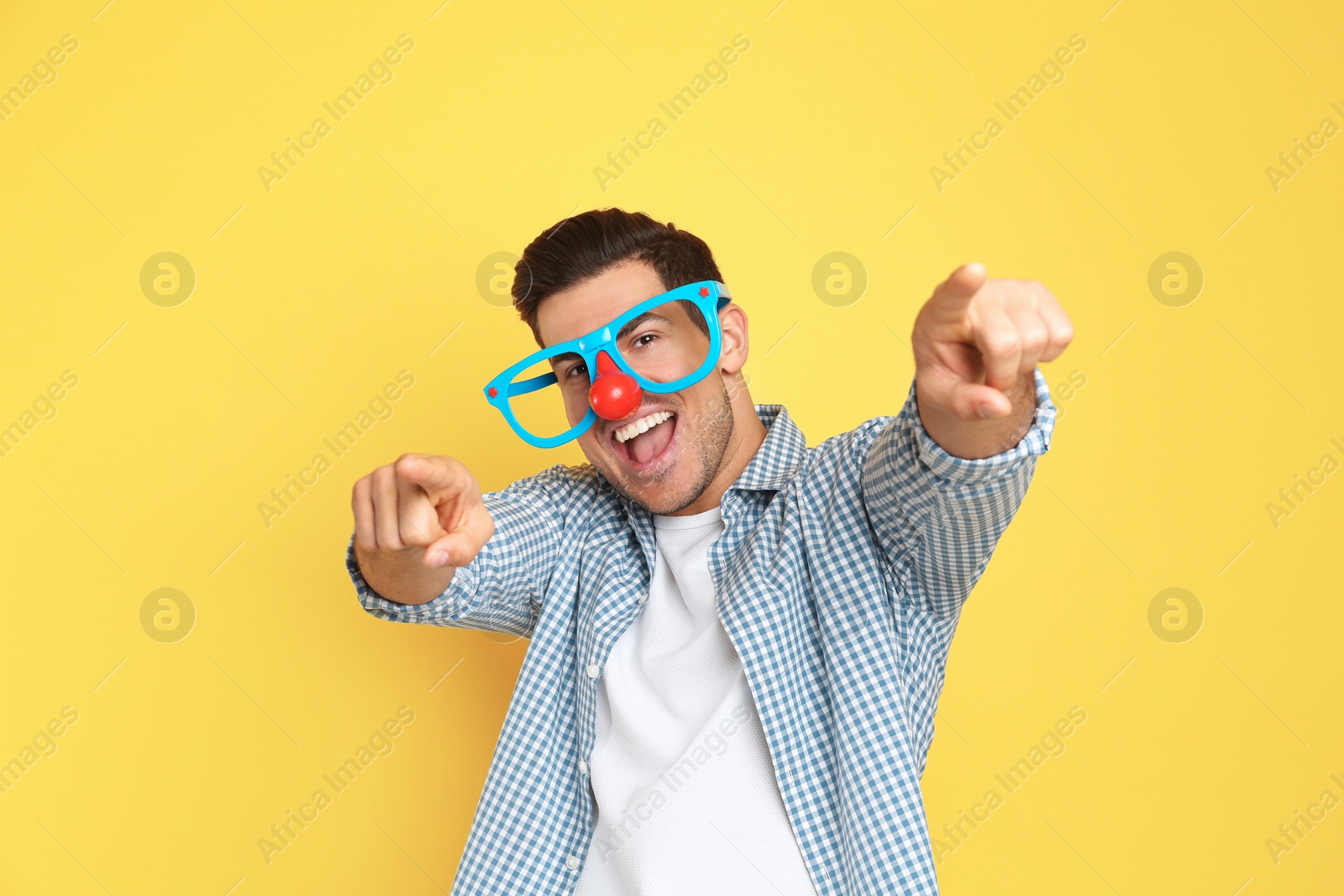 Photo of Joyful man with funny glasses on yellow background. April fool's day