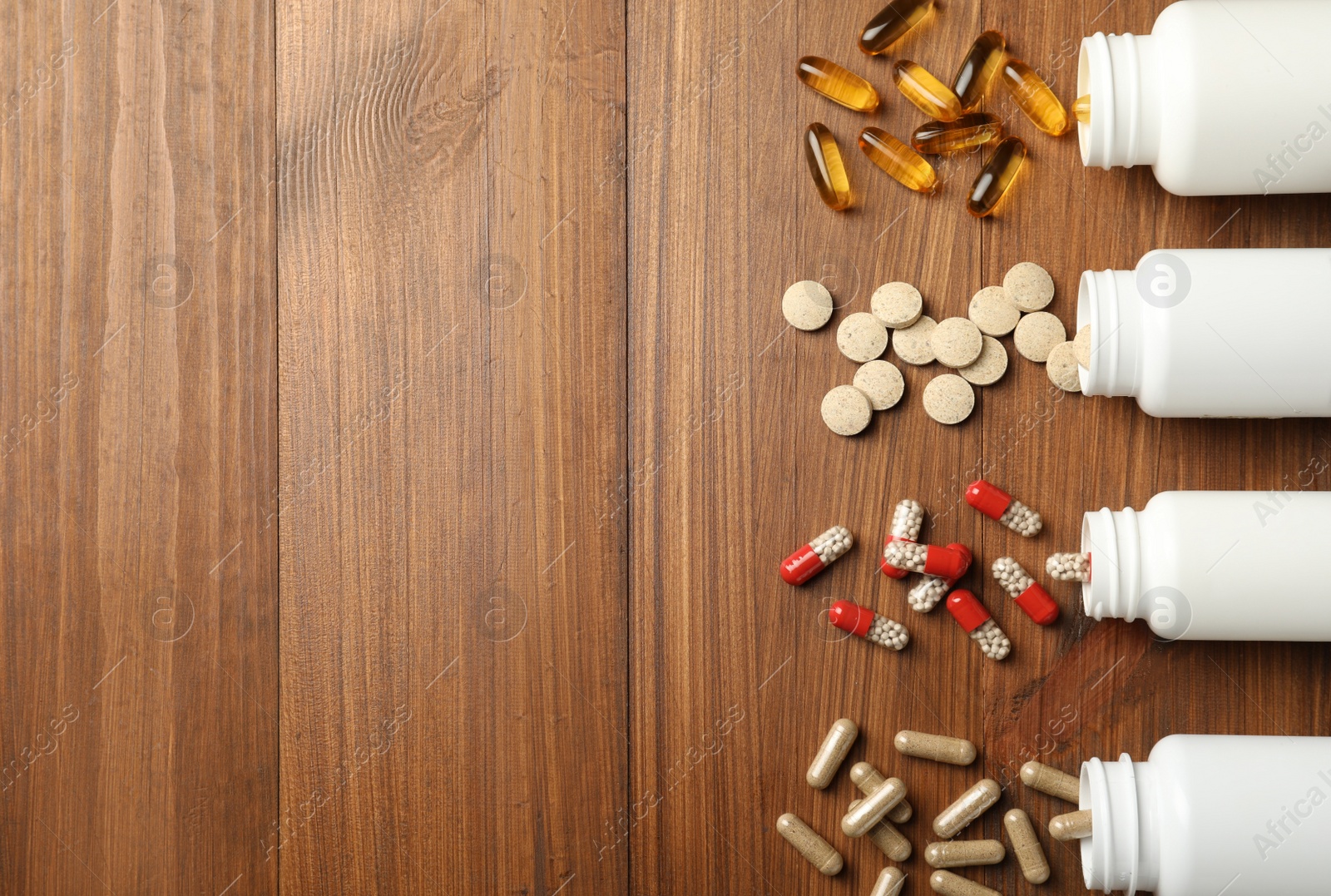 Photo of Overturned bottles with different dietary supplements on wooden table, flat lay. Space for text