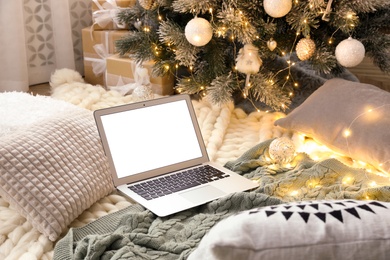 Photo of Modern laptop on plaid near Christmas tree