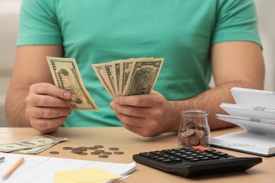 Photo of Young man counting money at wooden table indoors, closeup