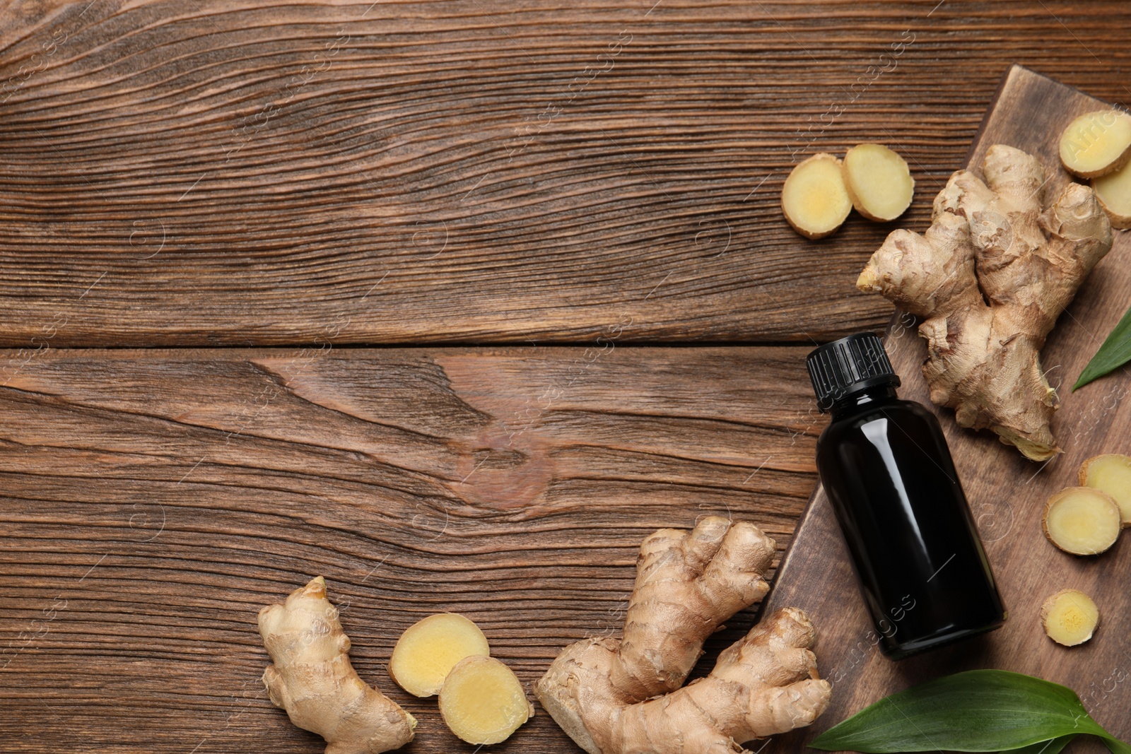 Photo of Glass bottle of essential oil and ginger root on wooden table, flat lay. Space for text