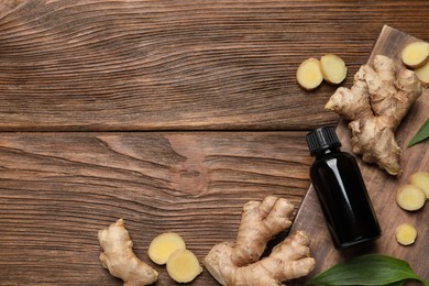 Glass bottle of essential oil and ginger root on wooden table, flat lay. Space for text