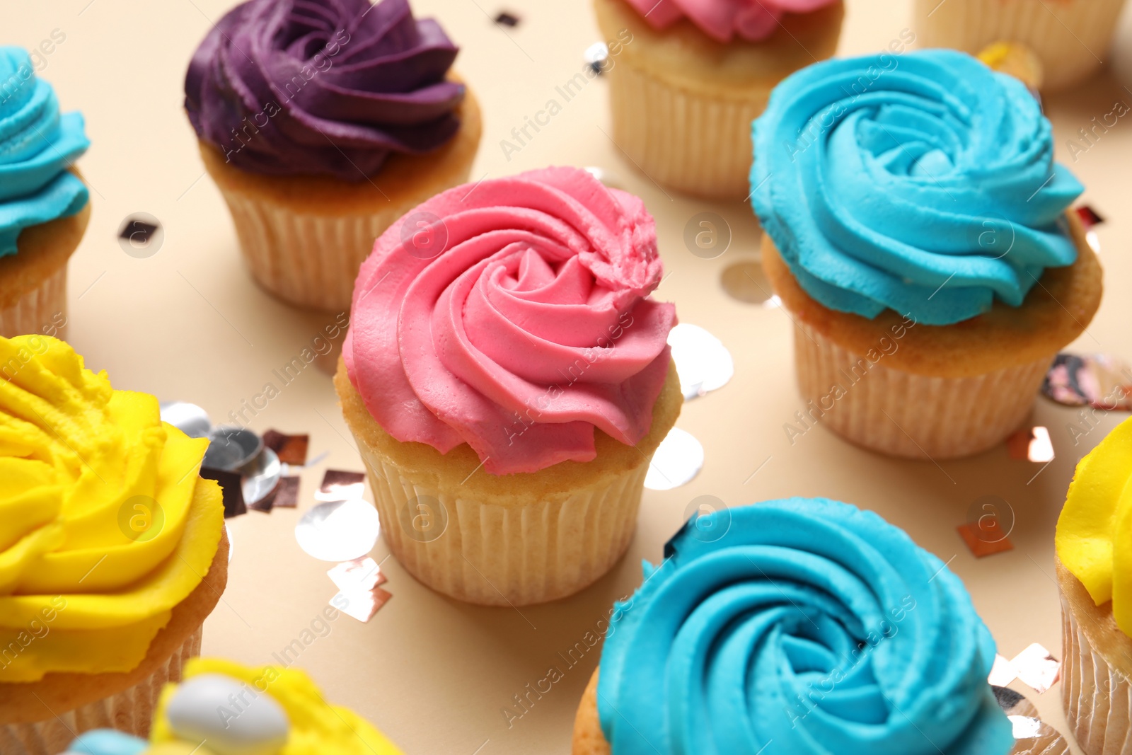 Photo of Delicious cupcakes with bright cream and confetti on beige background, closeup