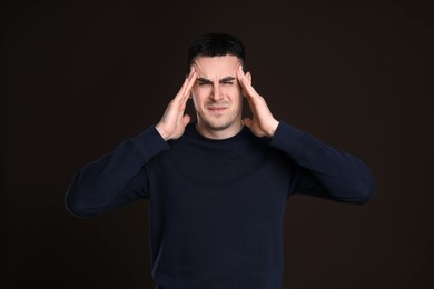 Young man suffering from headache on dark background. Cold symptoms