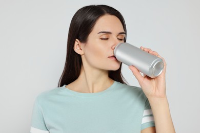 Photo of Beautiful young woman drinking from tin can on light grey background