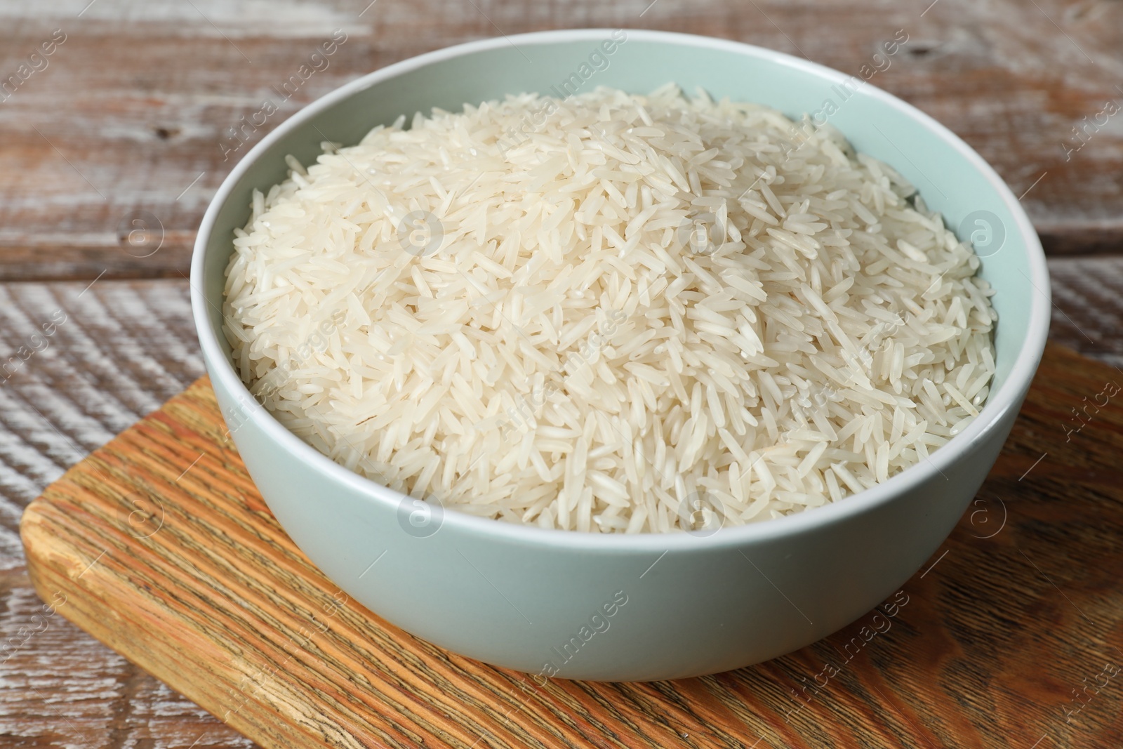 Photo of Raw basmati rice in bowl on wooden table, closeup