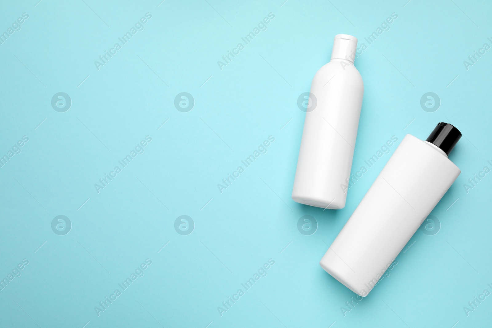 Photo of Bottles of shampoo on light blue background, flat lay. Space for text