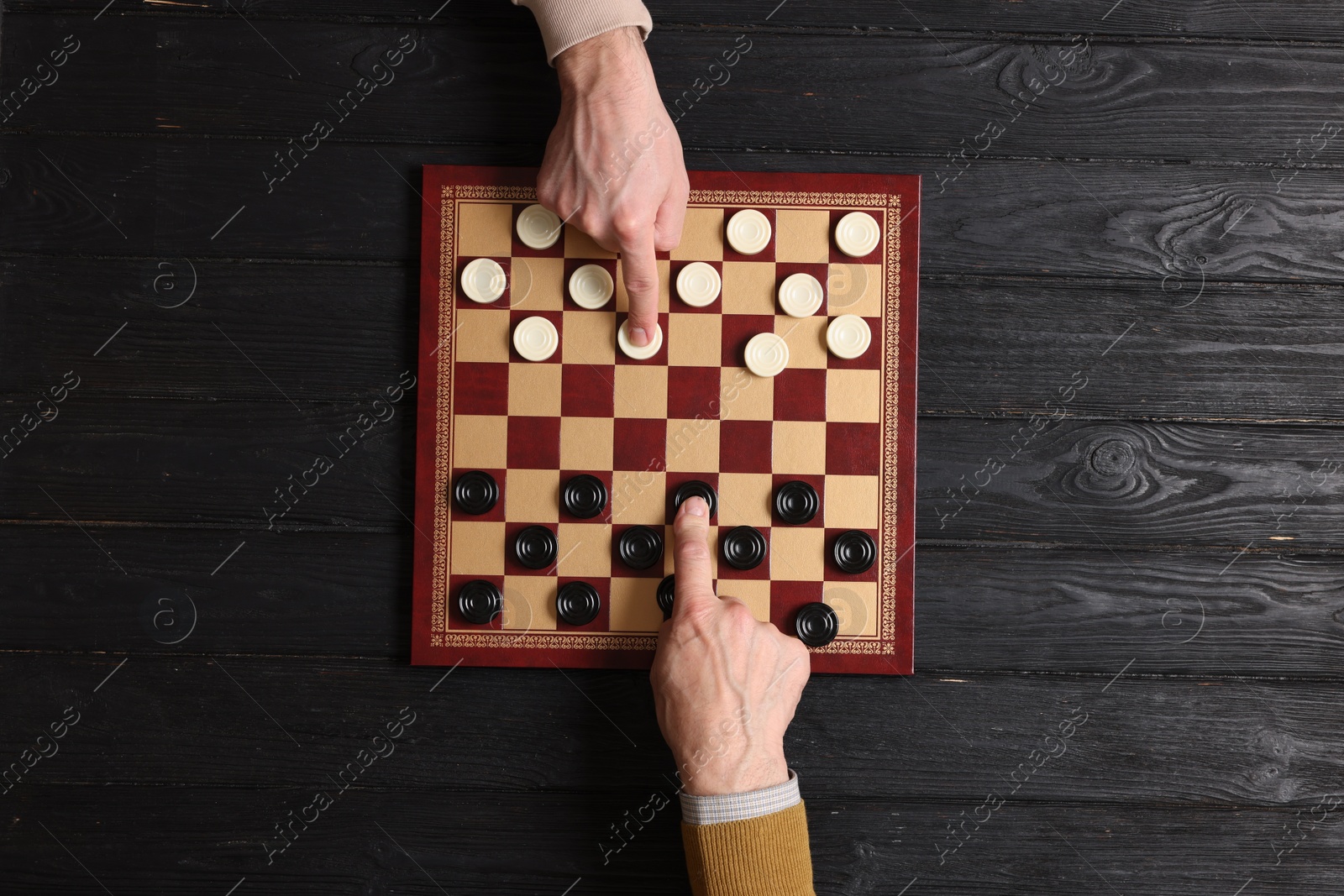 Photo of Man playing checkers with partner at black wooden table, top view