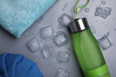 Bottle of water, ice cubes and towel on grey background, flat lay. Heat stroke treatment