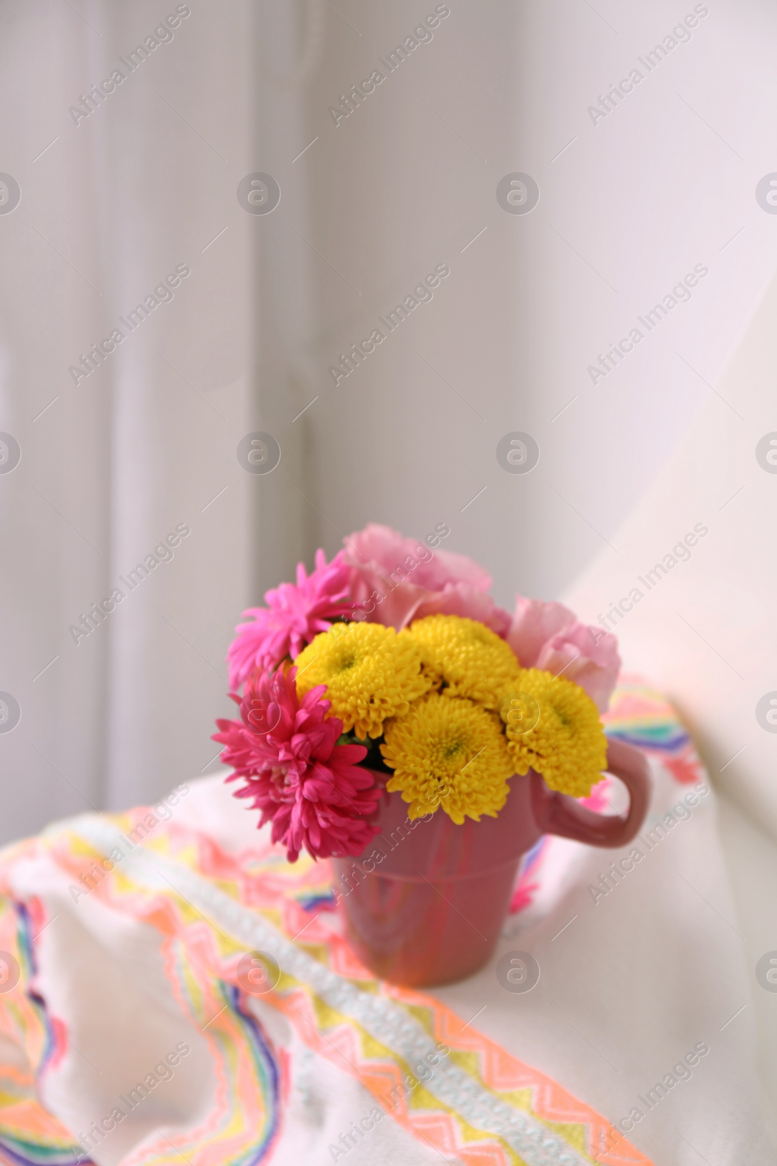 Photo of Beautiful bright flowers in pink cup and fabric on table indoors