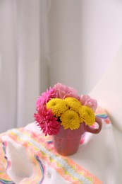 Beautiful bright flowers in pink cup and fabric on table indoors