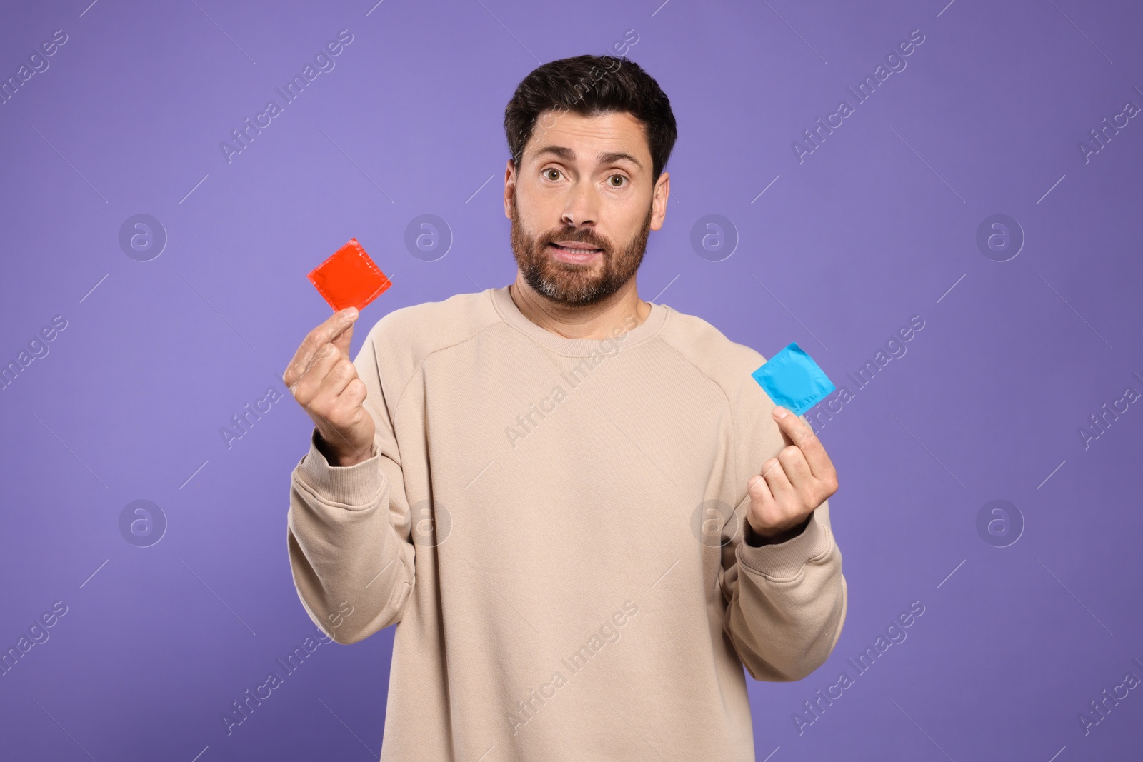 Photo of Confused man holding condoms on purple background. Safe sex