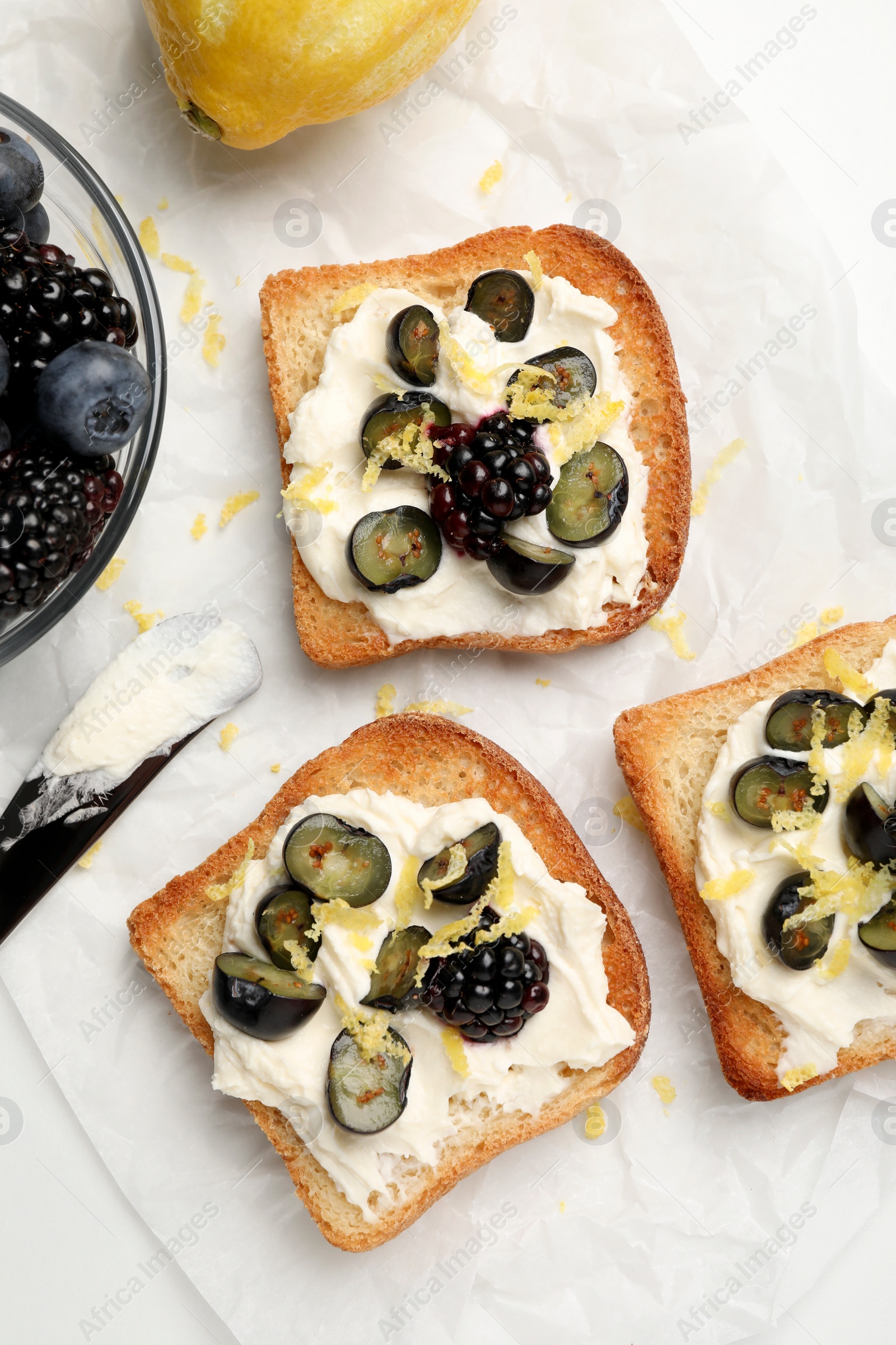Photo of Tasty sandwiches with cream cheese, blueberries, blackberries and lemon zest on white table, flat lay