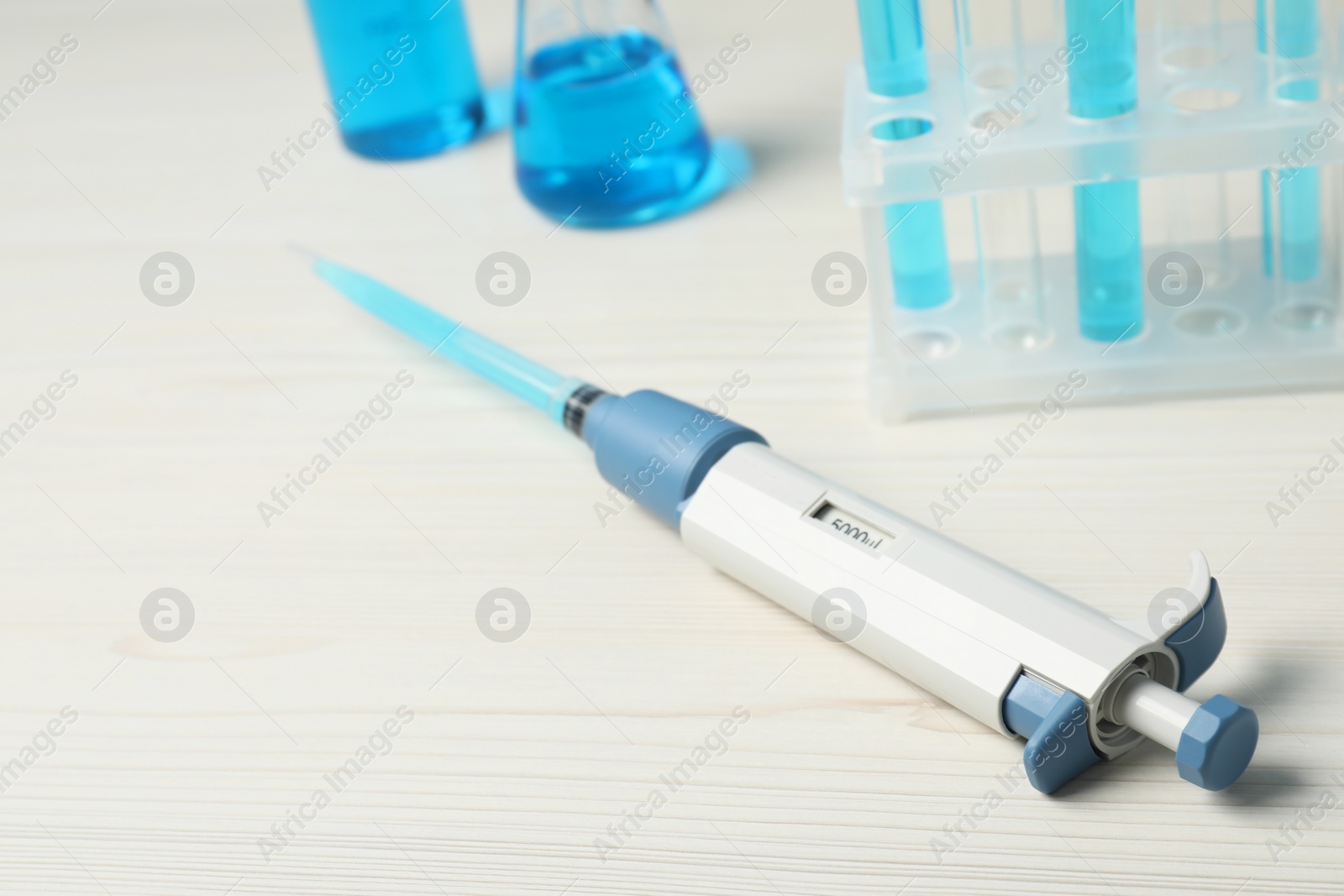 Photo of Laboratory analysis. Micropipette with liquid on white wooden table, closeup. Space for text