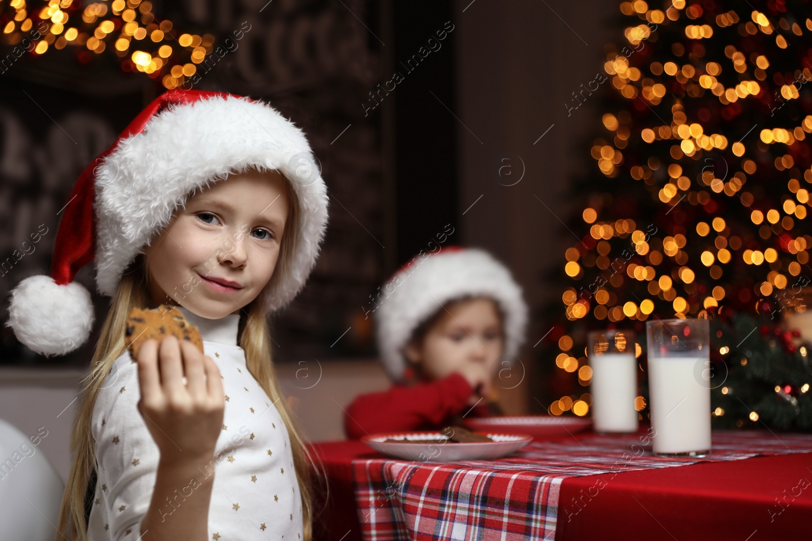 Photo of Cute little children eating cookies at table in dining room. Christmas time