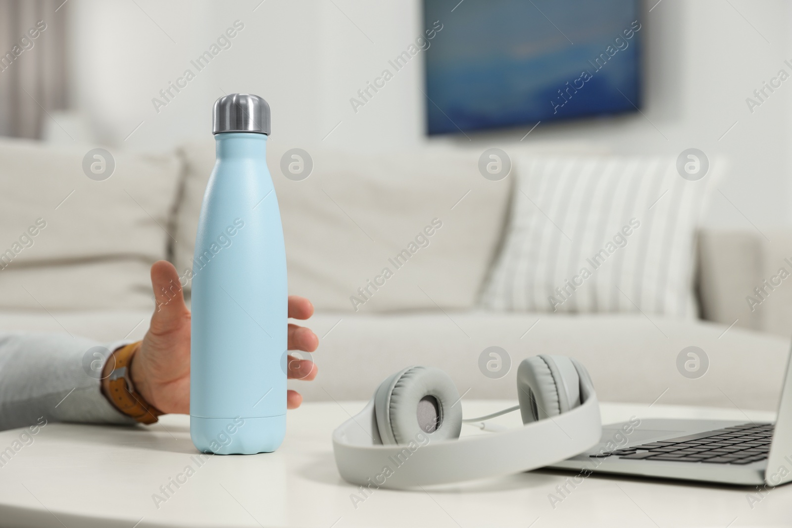 Photo of Man taking thermo bottle from white table at home, closeup