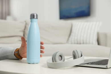 Photo of Man taking thermo bottle from white table at home, closeup