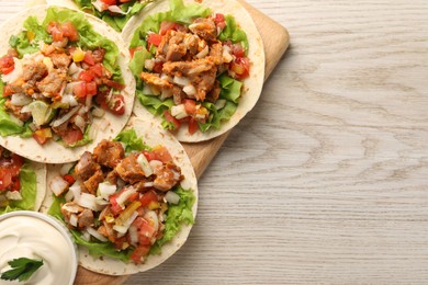 Delicious tacos with vegetables, meat and sauce on white wooden table, top view. Space for text