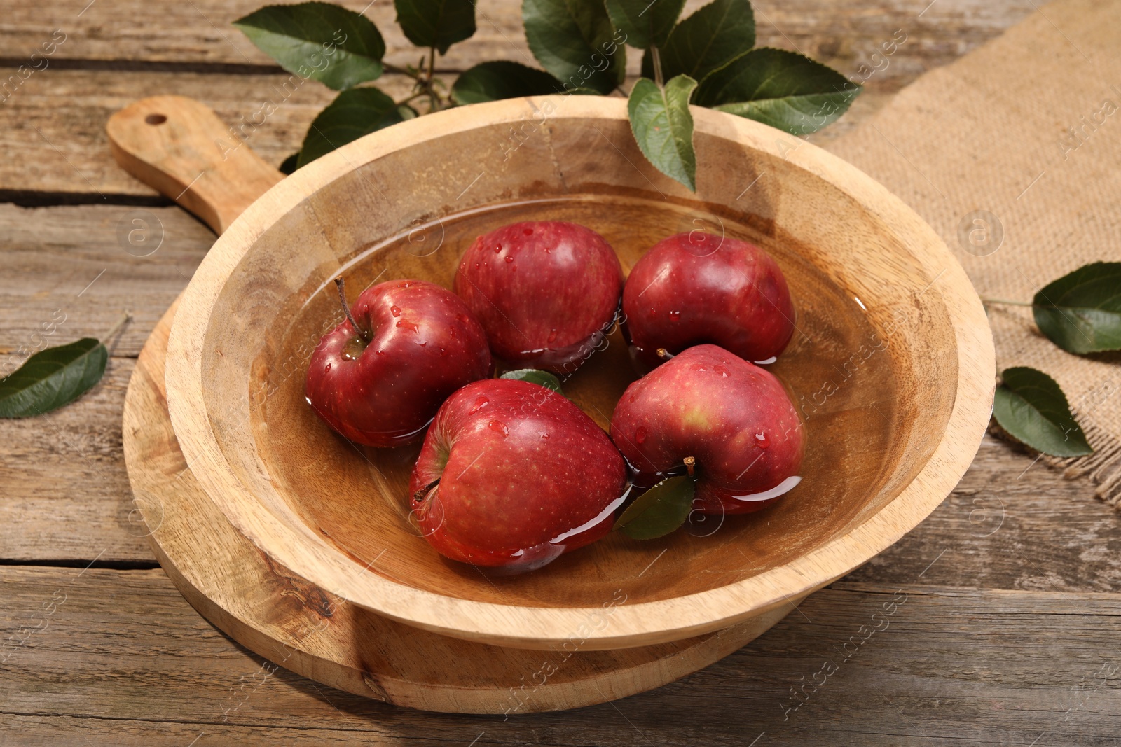 Photo of Fresh red apples in bowl with water and leaves on wooden table