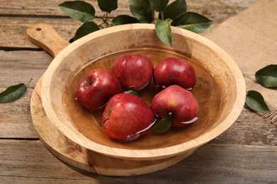 Photo of Fresh red apples in bowl with water and leaves on wooden table
