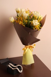 Bouquet with beautiful spring flowers and necklace on wooden table