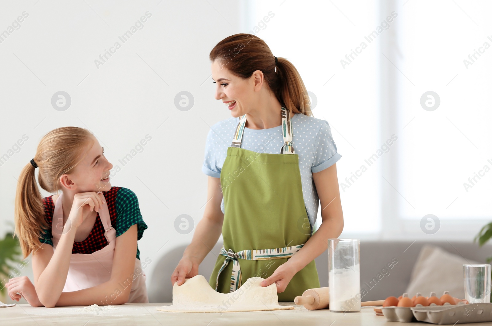 Photo of Mother and her daughter making dough at table in kitchen