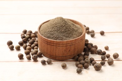 Photo of Ground and whole allspice berries (Jamaica pepper) in bowl on light wooden table, closeup