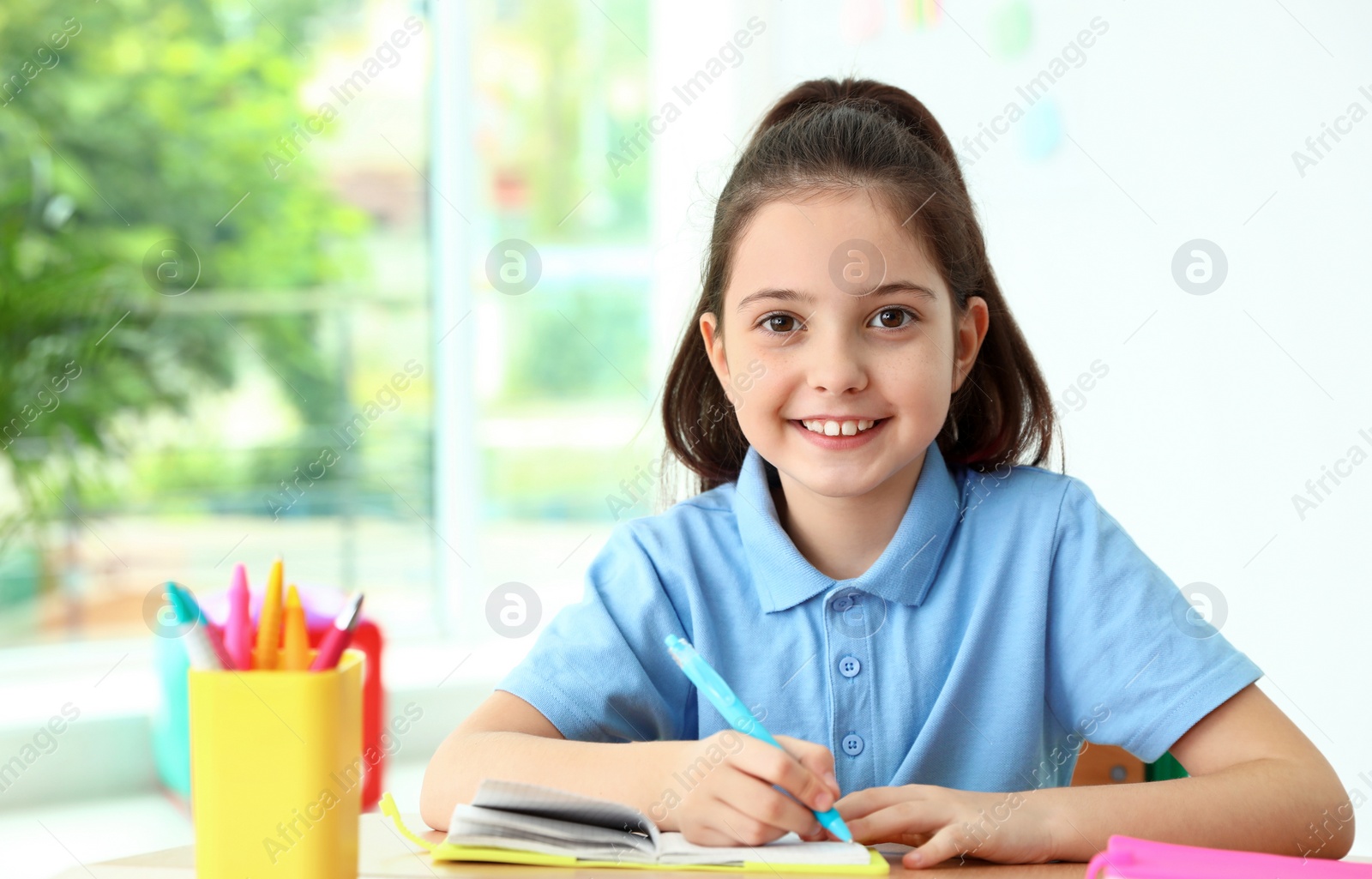 Photo of Little girl doing assignment at desk in classroom. School stationery