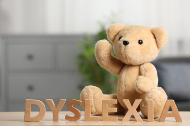 Photo of Teddy bear and word Dyslexia made of letters on wooden table indoors