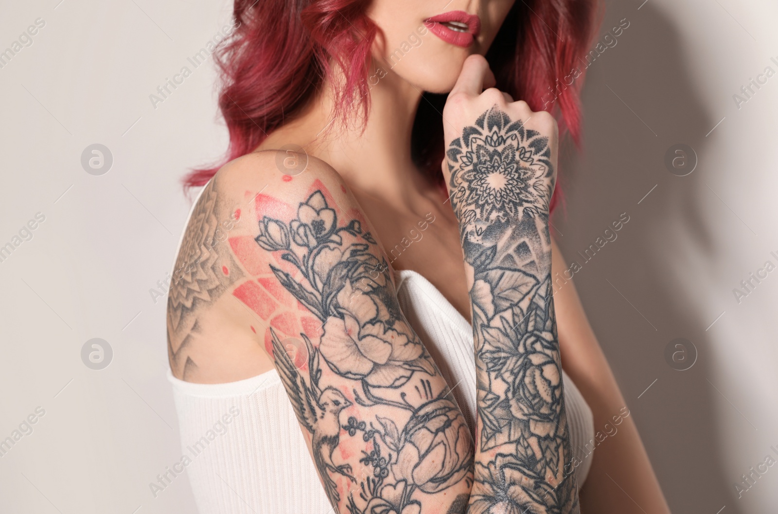 Photo of Beautiful woman with tattoos on body against light background, closeup