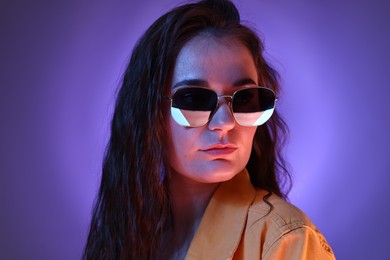 Portrait of beautiful young woman with stylish sunglasses on color background with neon lights