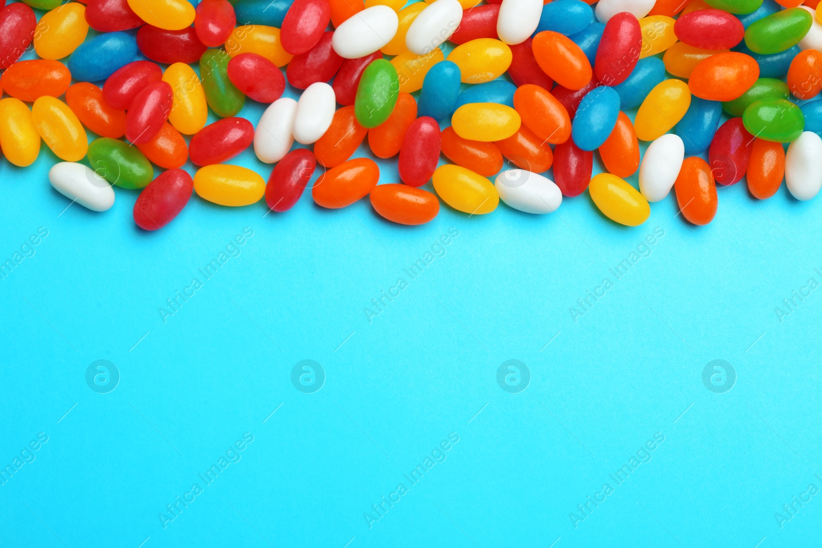 Photo of Tasty colorful jelly beans on blue background, flat lay. Space for text