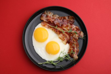 Photo of Fried eggs, bacon and microgreens on red background, top view