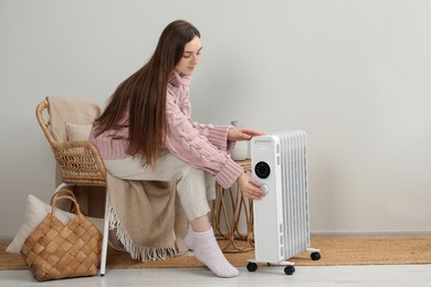 Photo of Young woman adjusting temperature on modern portable electric heater indoors