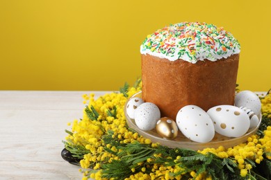 Traditional Easter cake with sprinkles, painted eggs and beautiful spring flowers on white wooden table, space for text