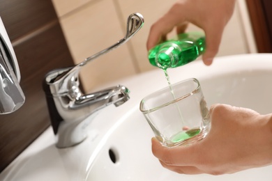 Photo of Man pouring mouthwash from bottle into glass in bathroom, closeup. Teeth care